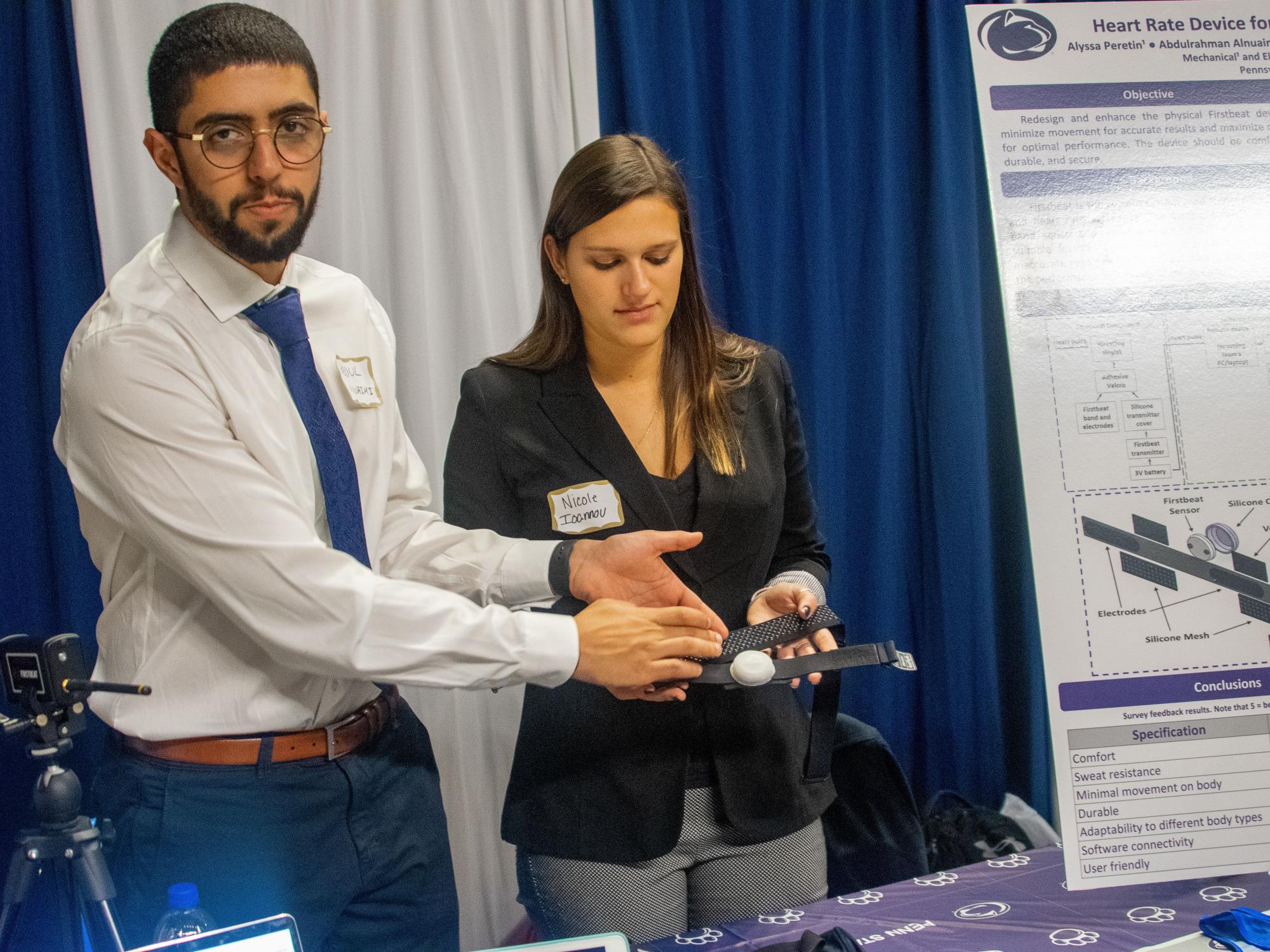 two students standing beside poster, present model of project