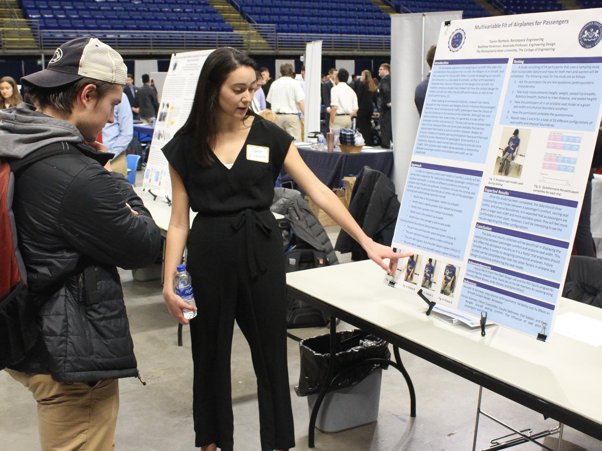 female student points to poster, explaining project to male student