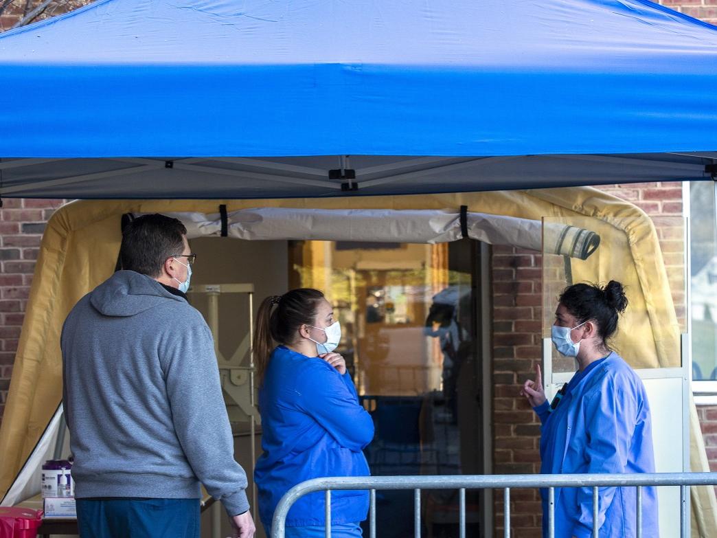 One man and two women radiologic technologists stand under a tent outside the Radiology Annex. The man is wearing a sweatshirt, and the women are wearing scrubs. All three are wearing face masks. The tent is open on all four sides.