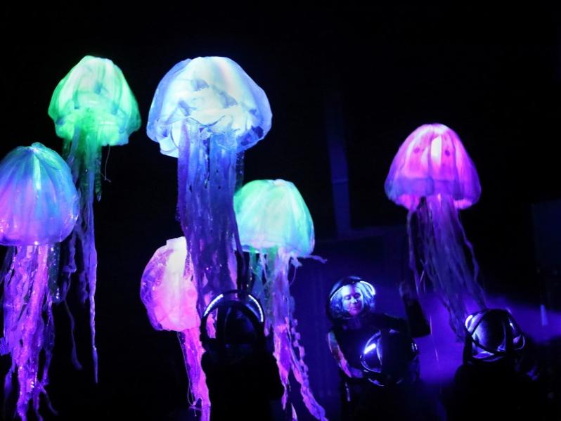 A woman stands amid glowing objecs resembling jellyfish.