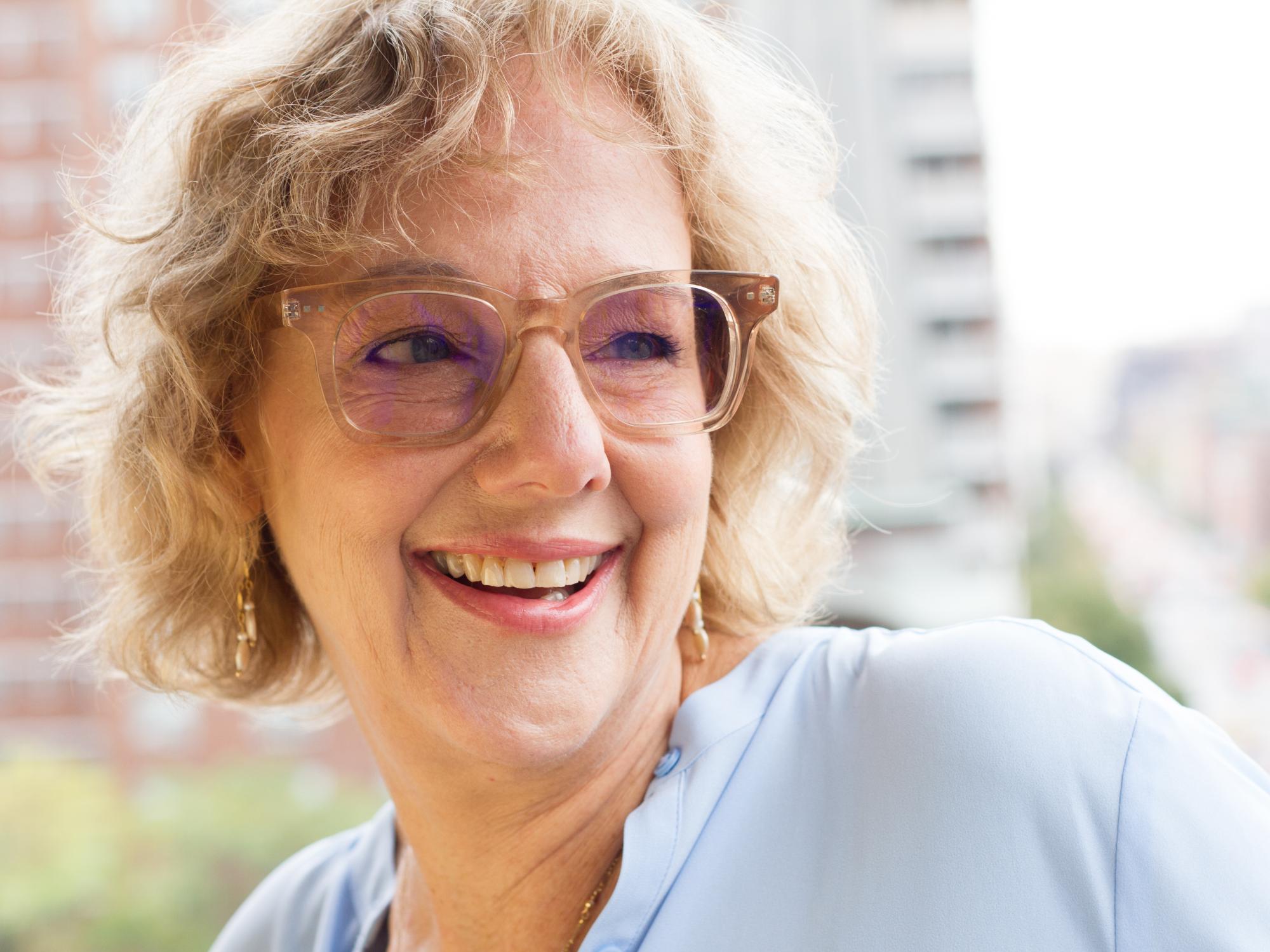 A woman wearing glasses with tinted lenses smiles and looks off to her left.