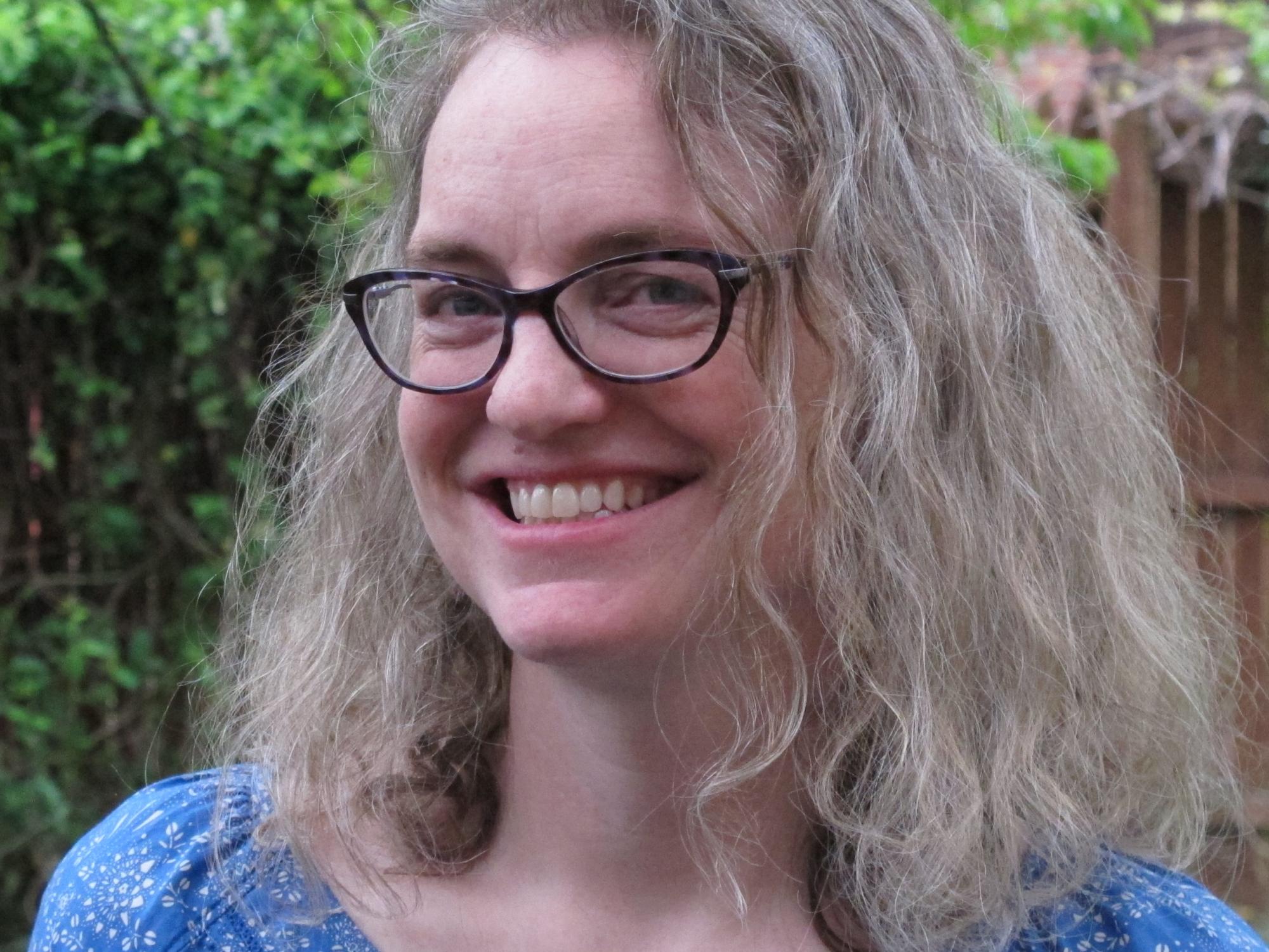 outdoor photo portrait of woman's head and shoulders; she is wearing black glasses and blue print shirt