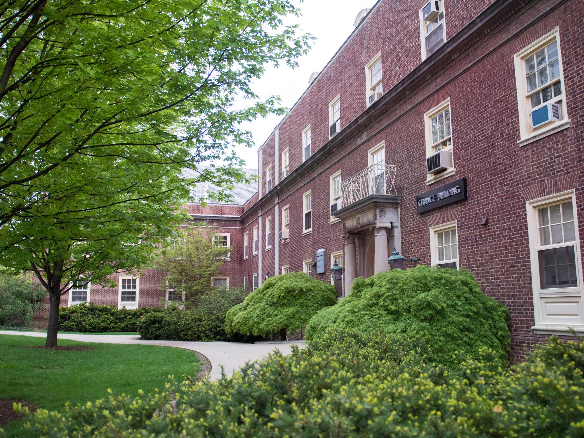 exterior of brick building with lawn, tree, bushes in front