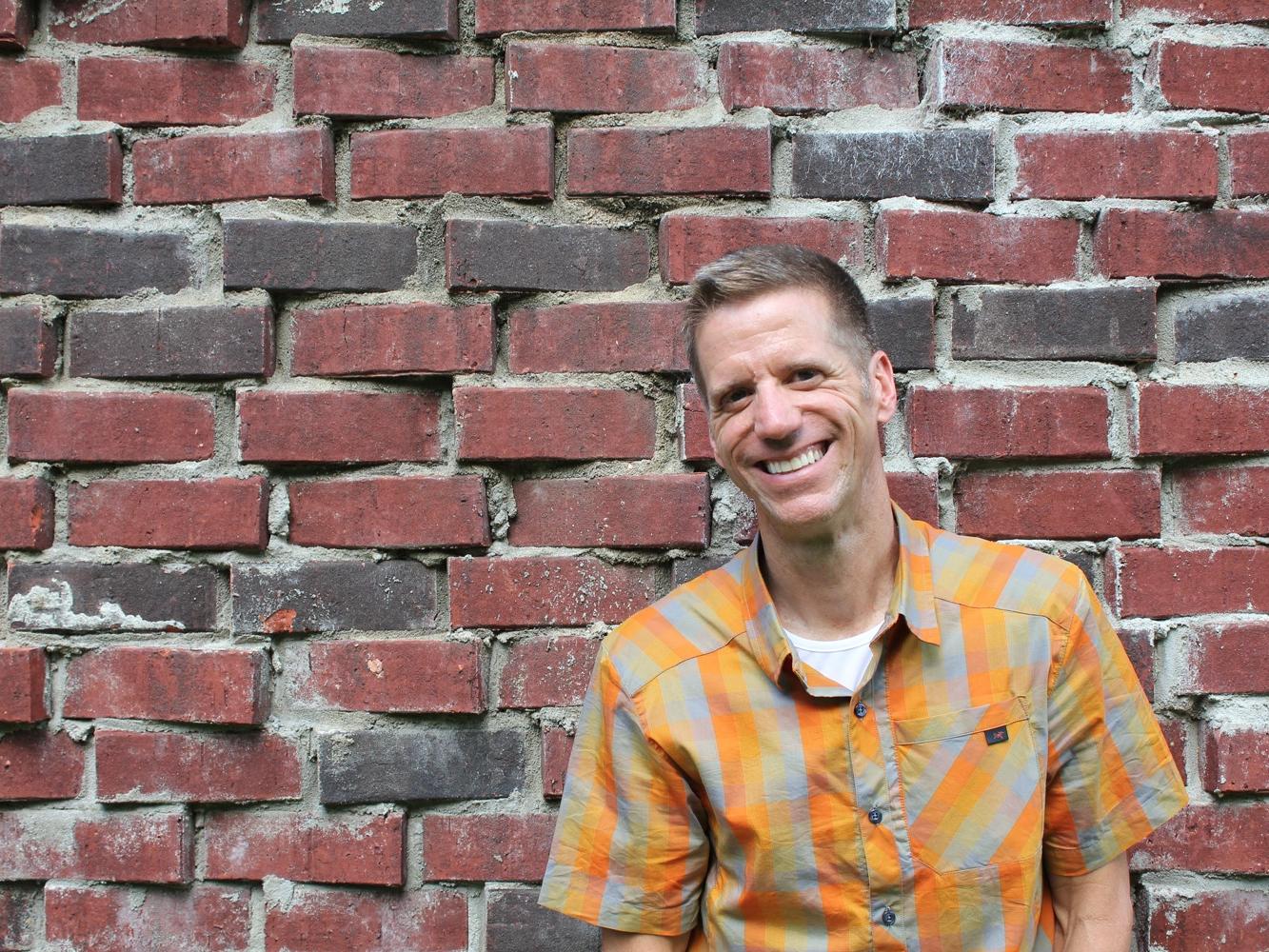Image of man smiling for camera in front of brick wall