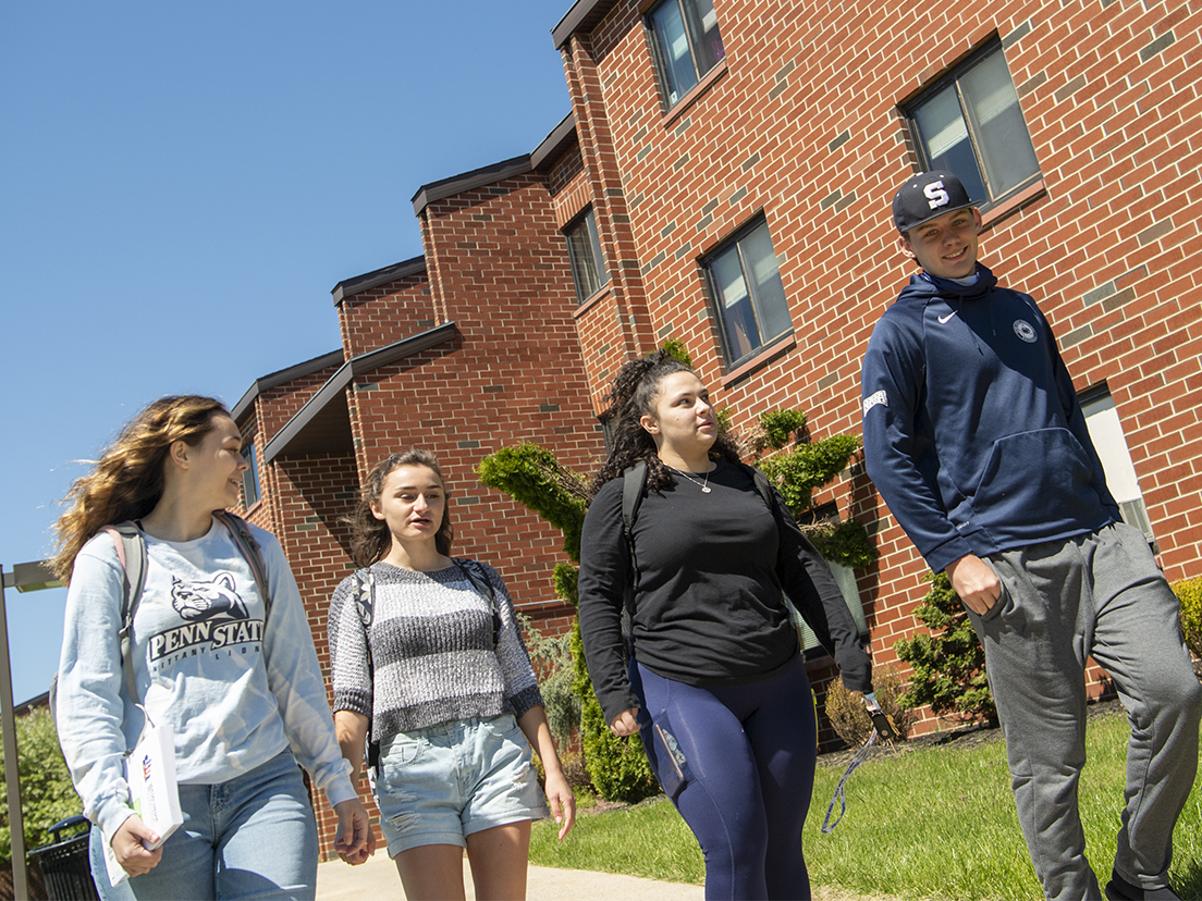 Four students walk together outside of student housing complex.