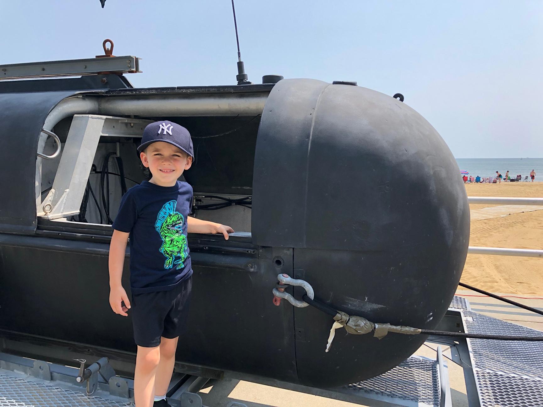 A young boy wearing a Yankees hat stands outside of a submersible and smiles for the camera.