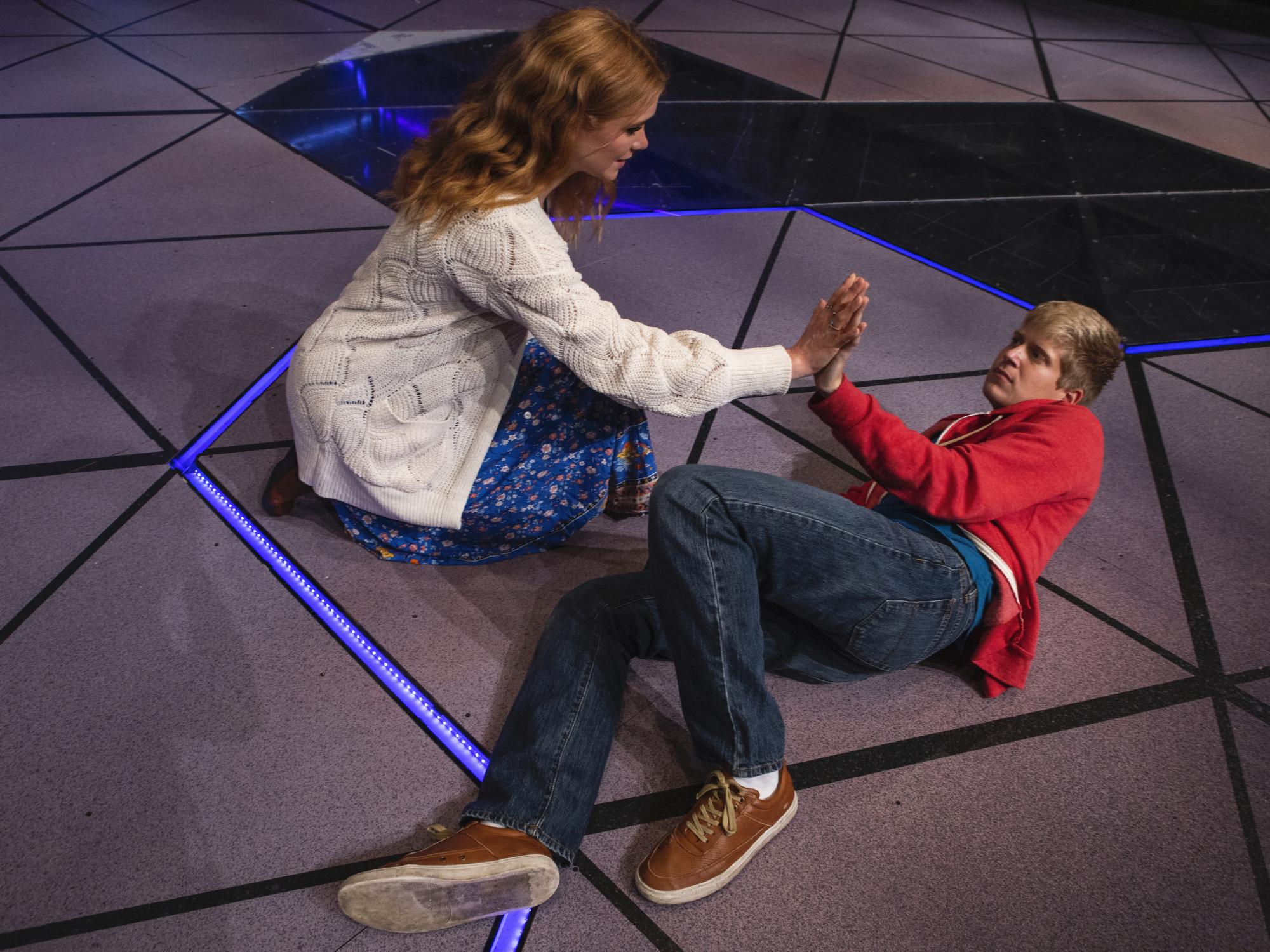 Two people touch hands, while one lies on the floor. 