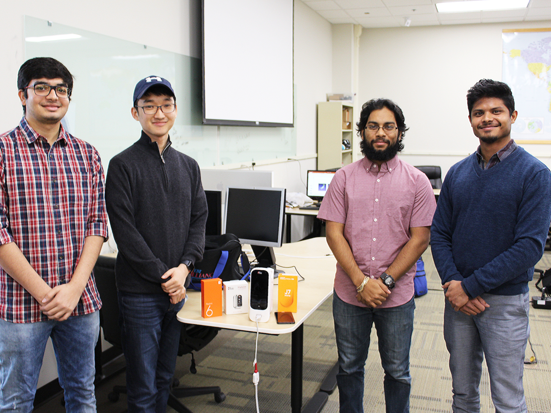 Four students standing near a desk with cell phone equipment on it
