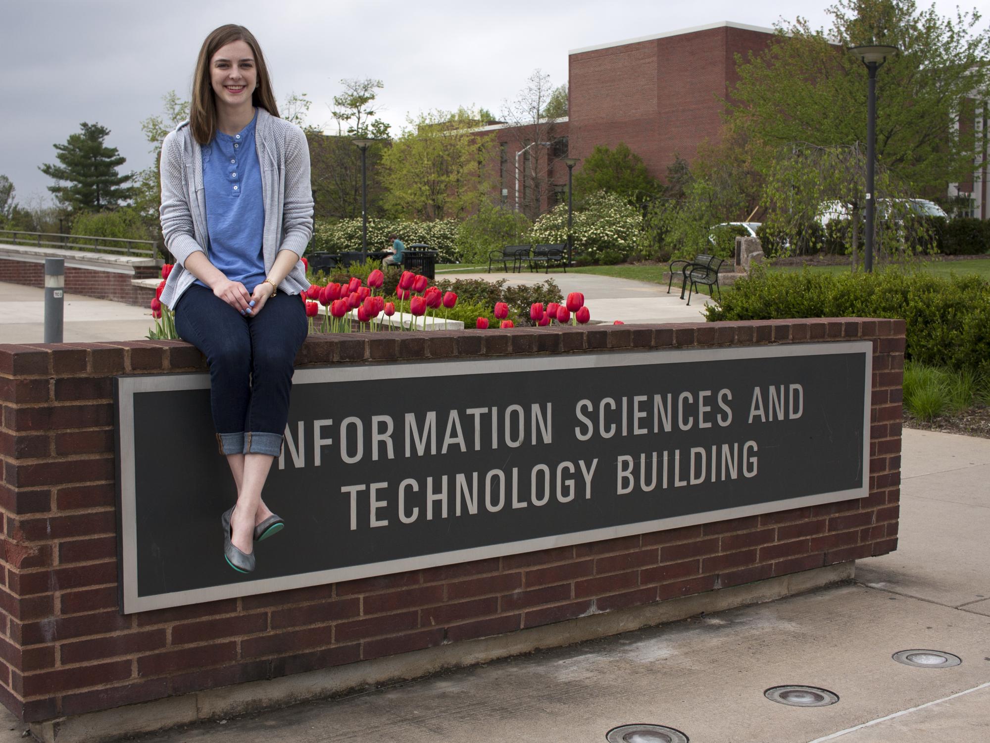 Audra Stafursky sits on the sign for the Information Sciences and Technology Building