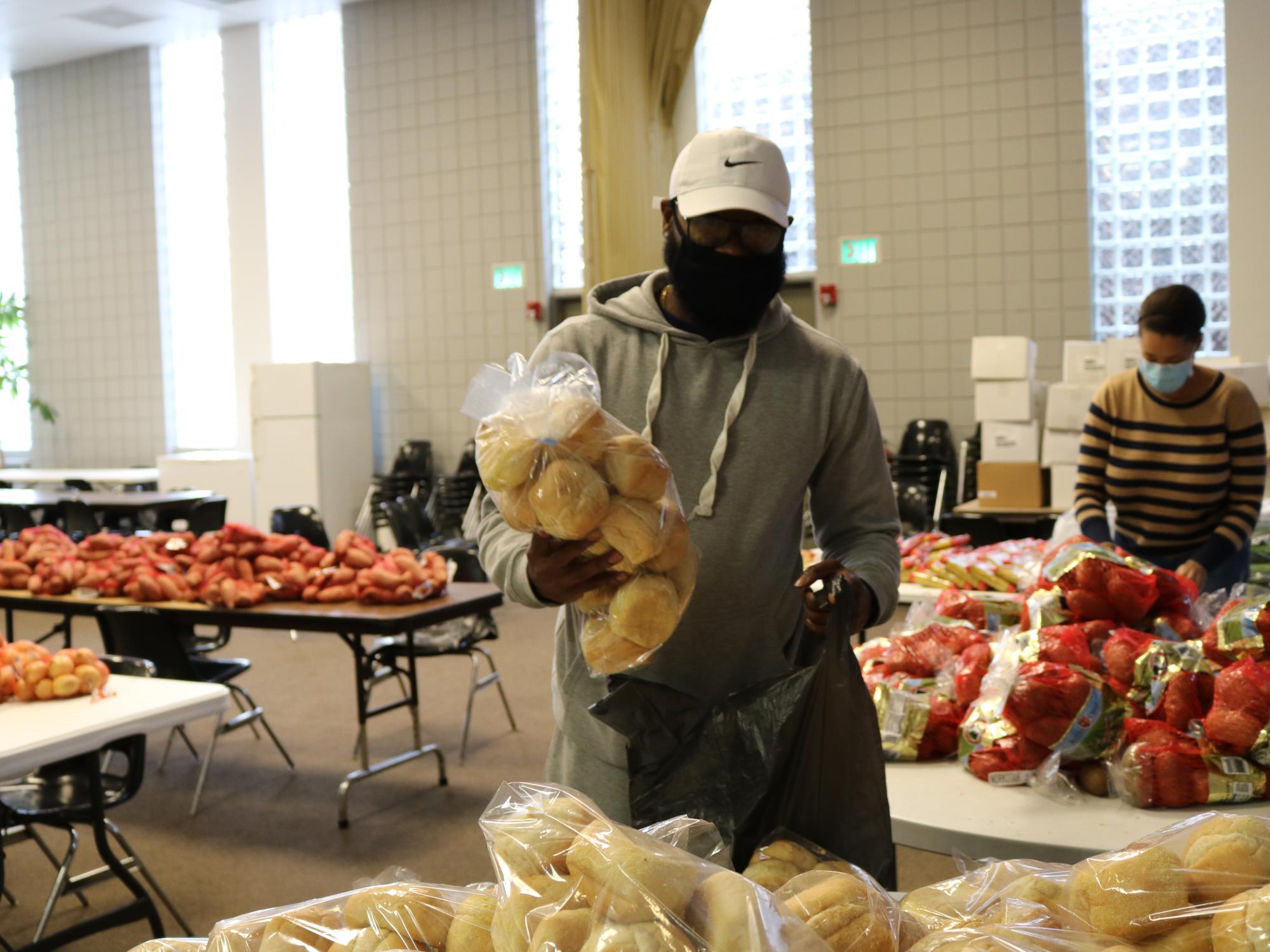 Man holding a package of rolls, preparing to place them into a plastic bag.