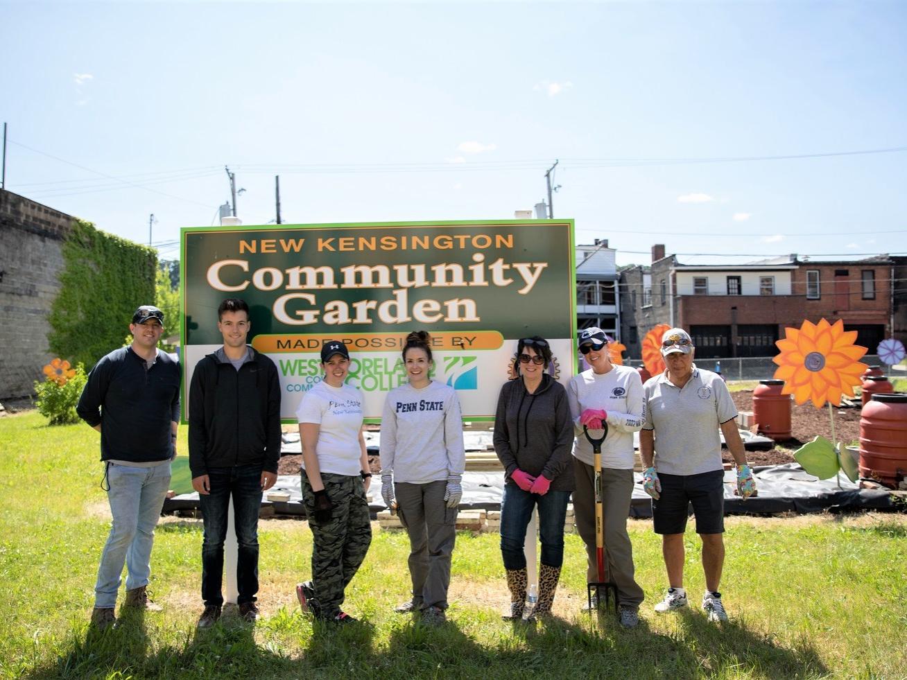 Seven men and women stand in community garden