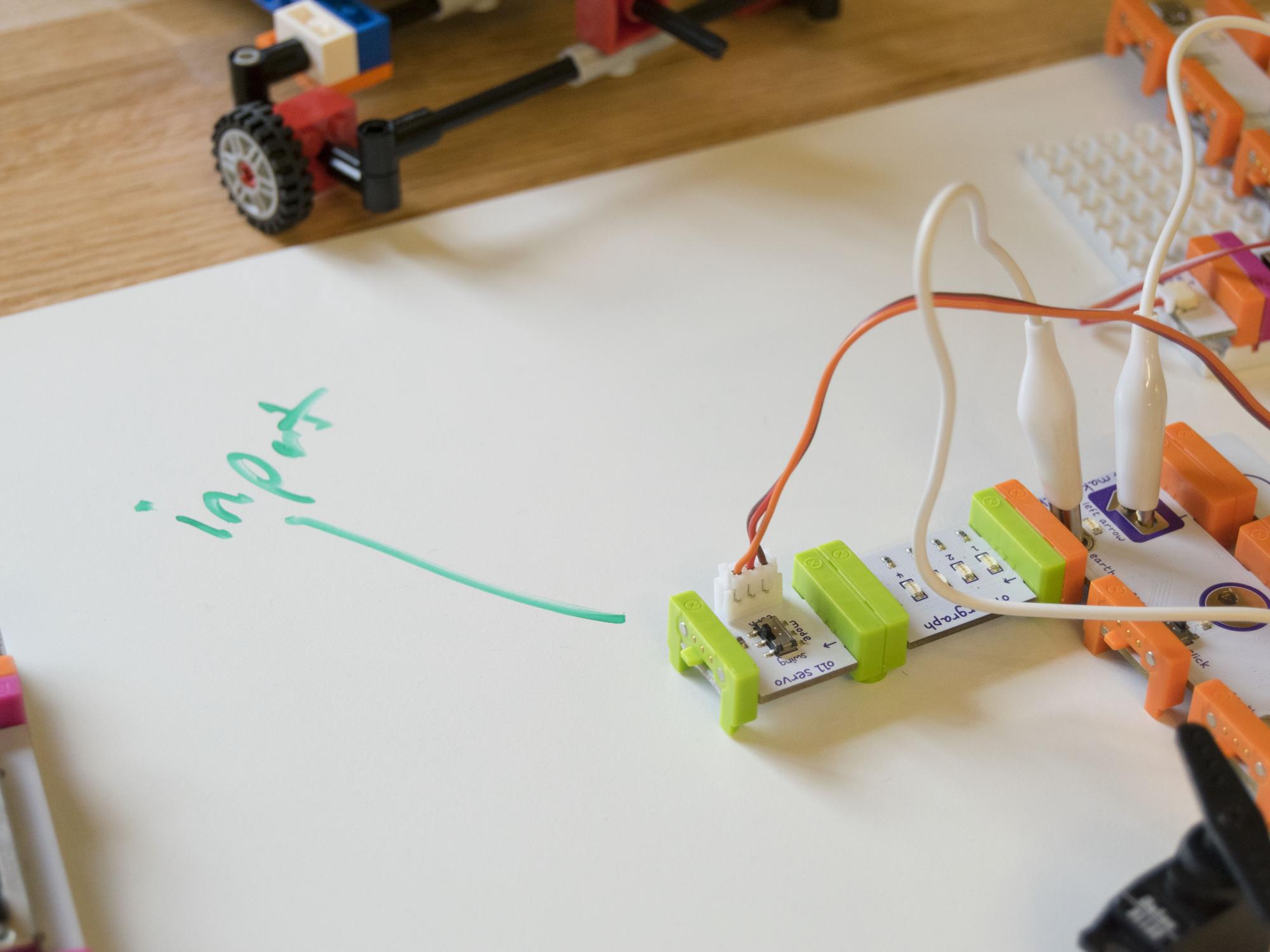 LittleBits rest on the dry-erase panel of a table with the word "input" written on it and pointing to a littleBit.