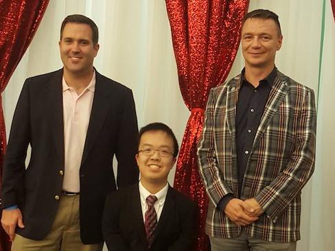 A man of short stature stands with two men, all wearing suits. 