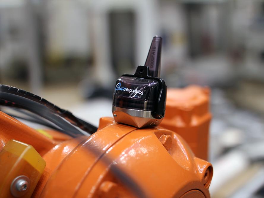 A small, black sensor sits on top of an orange machine.