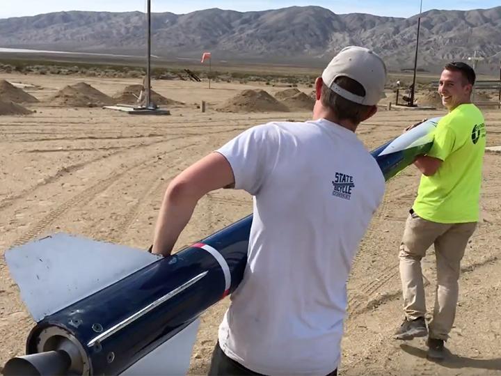 Two of the team members carry the rocket to the launch pad