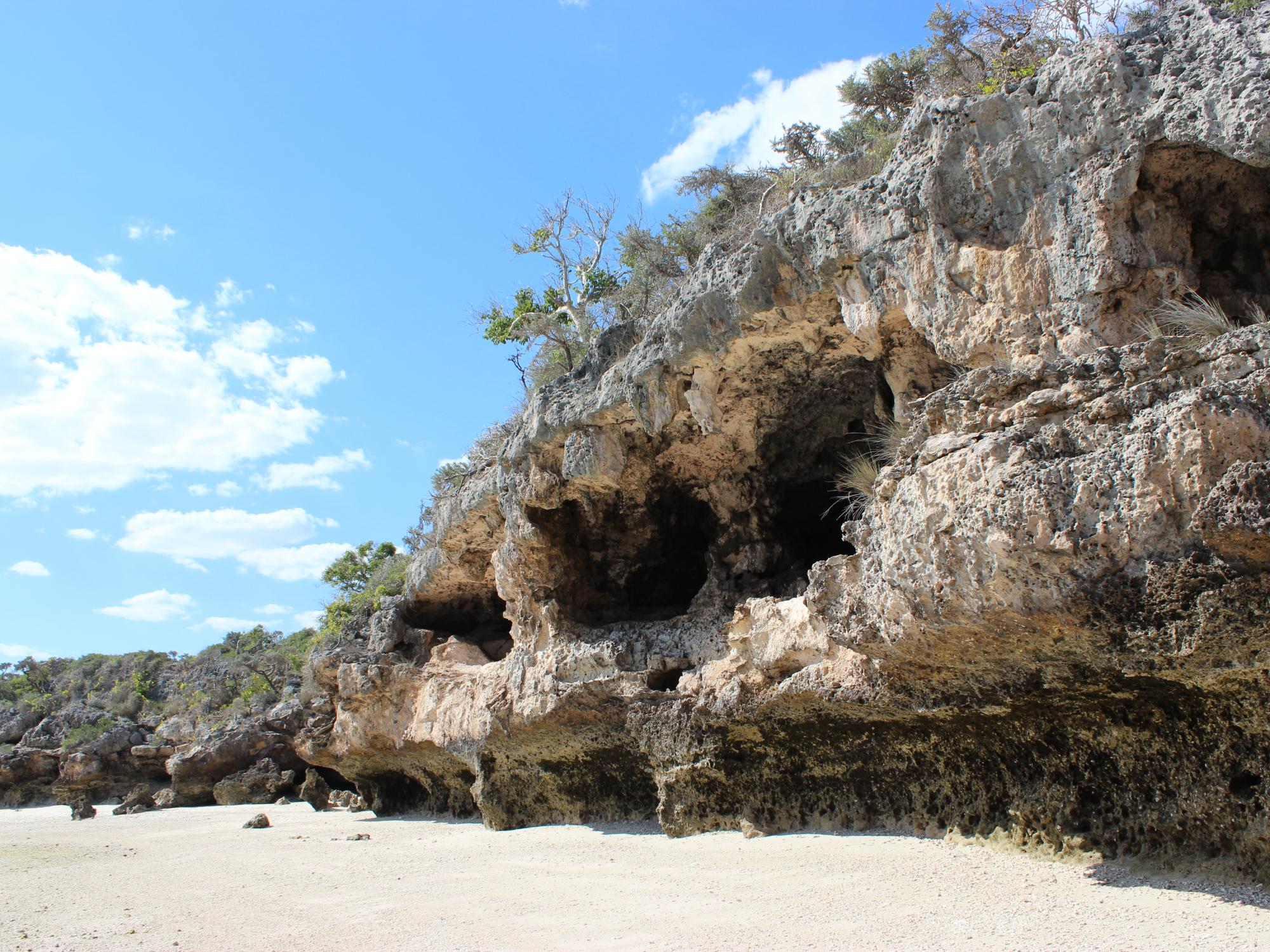 Rocky cliff with three caves in the side behind a sand beach