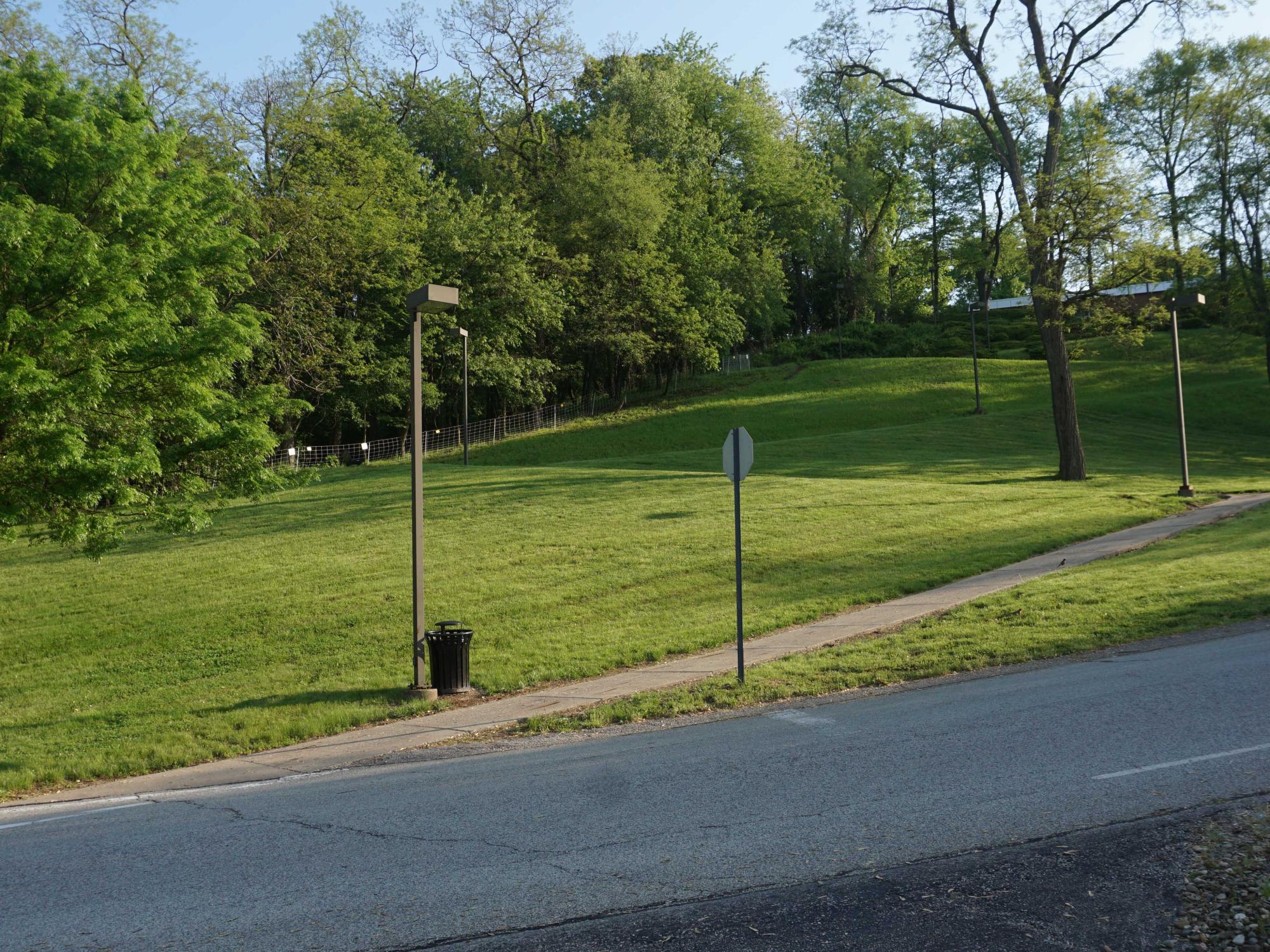 a road way in the foreground. In the back ground there is a hill with a walking path and lighting