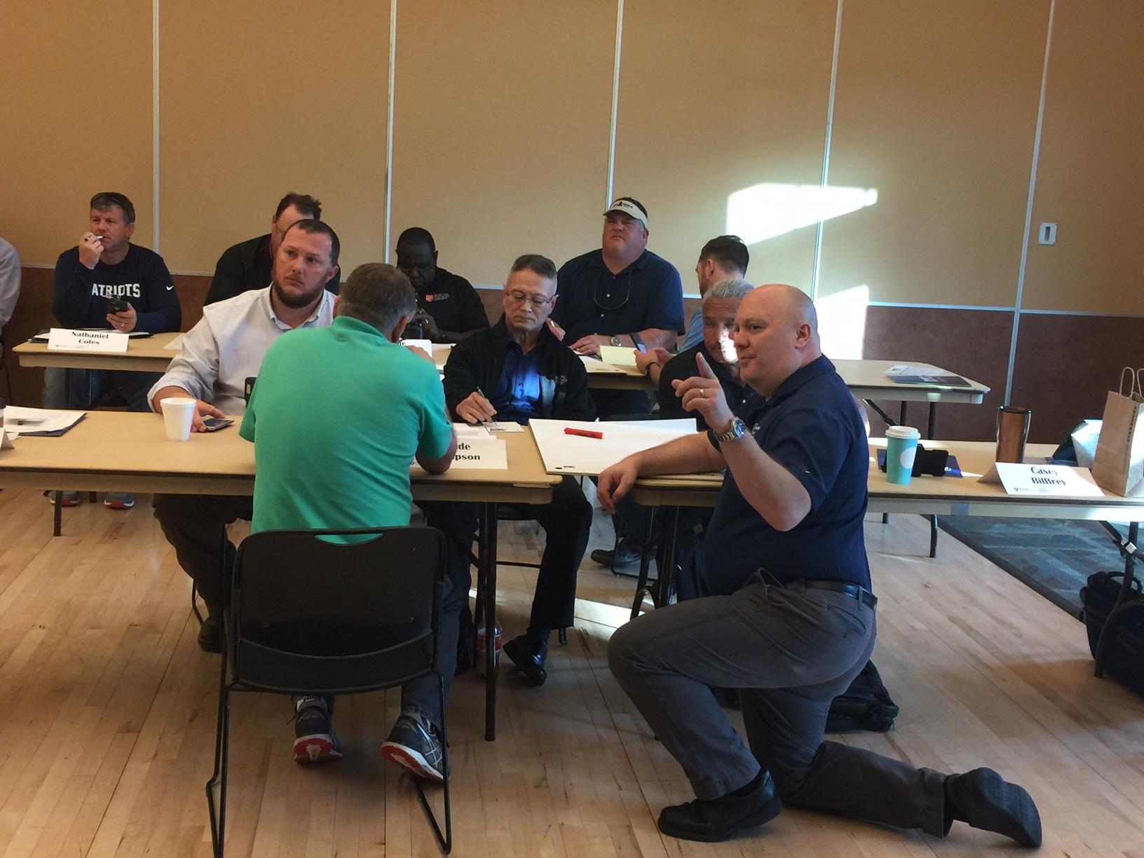 Man on knee explains subject matter to students
