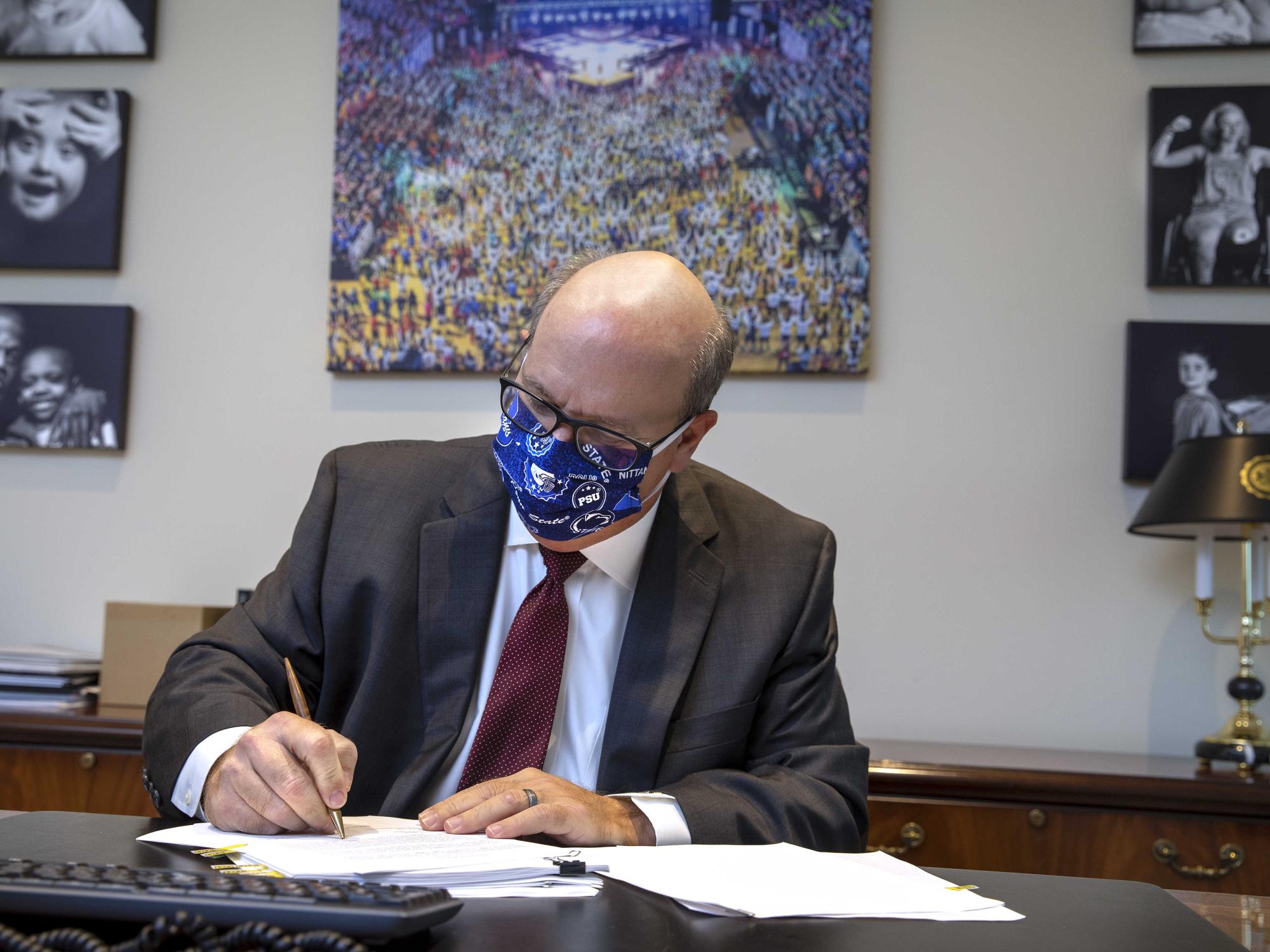 Steve Massini, Penn State Health CEO, is seated at his office desk, signs a document.