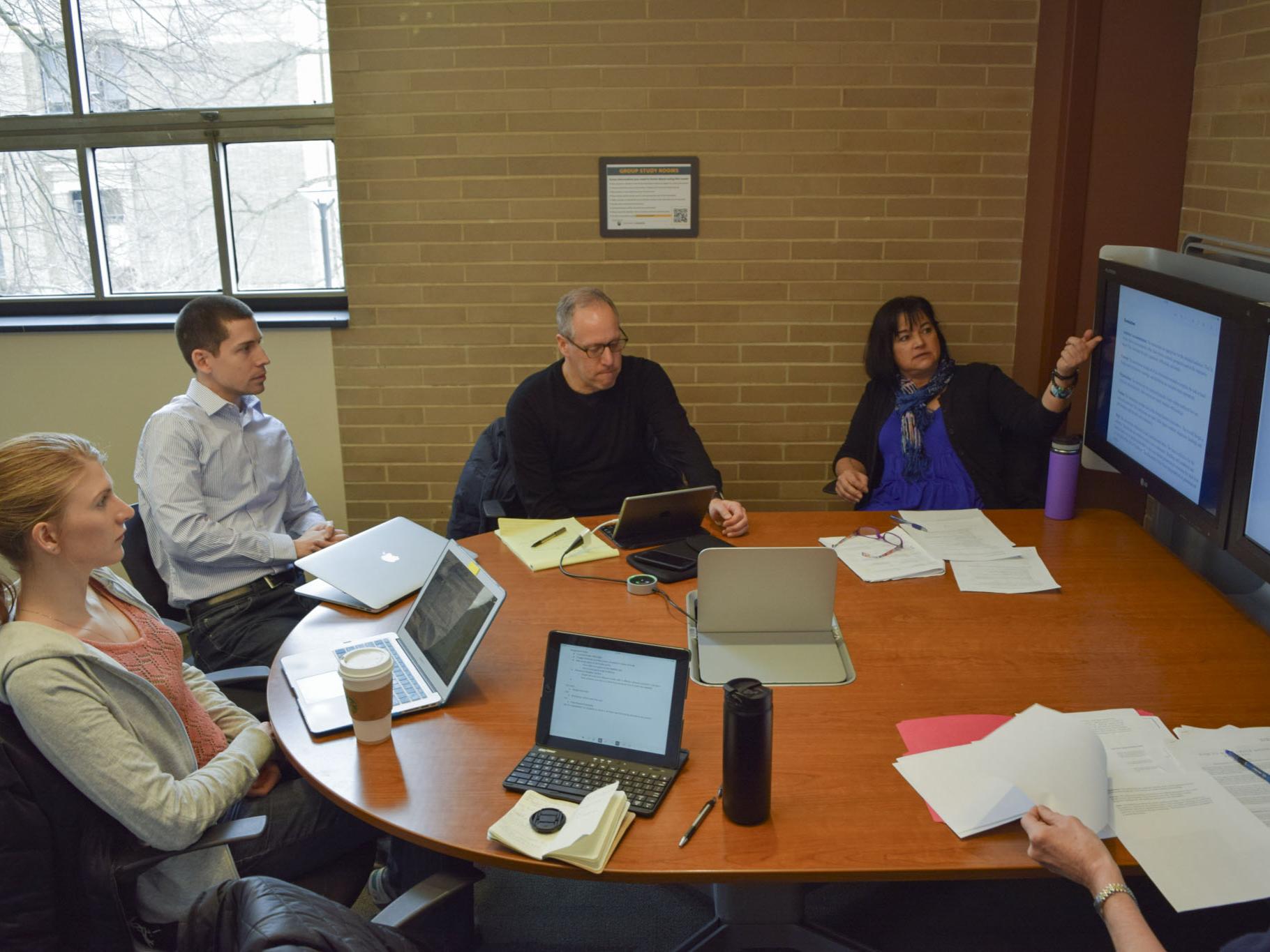 Staff members sit around a table in front of a screen