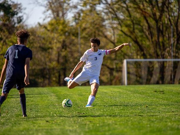 Male soccer player kicks ball on field