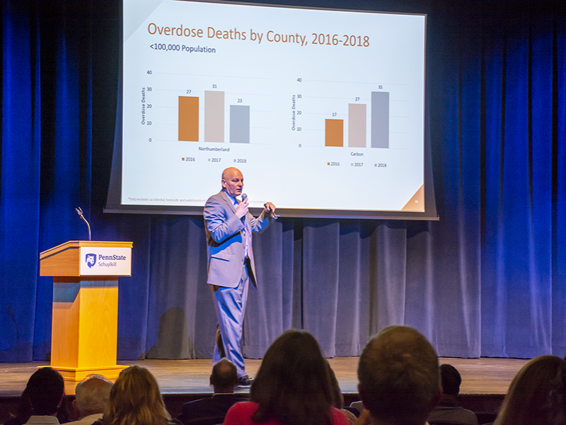 Schuylkill County District Attorney Mike O'Pake delivers a presentation, standing in front of a slide that examines drug overdose deaths by county between 2016-18