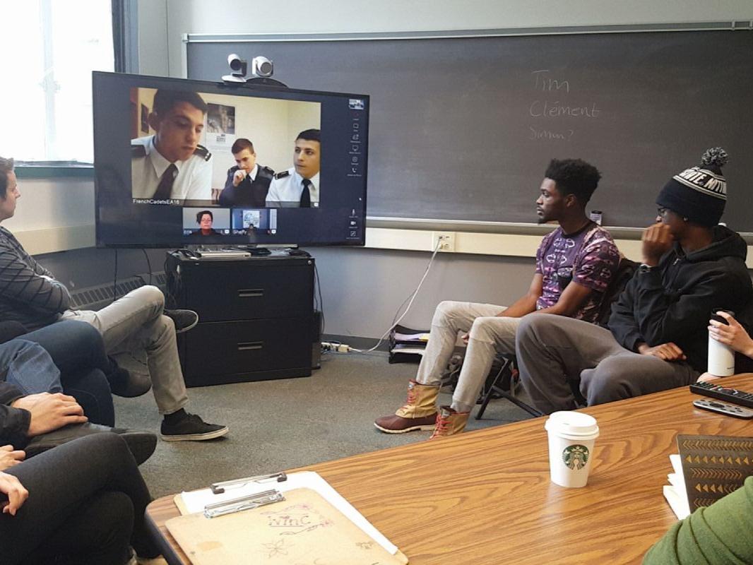 Student facilitators gathered around a television for a Skype session with French military cadets