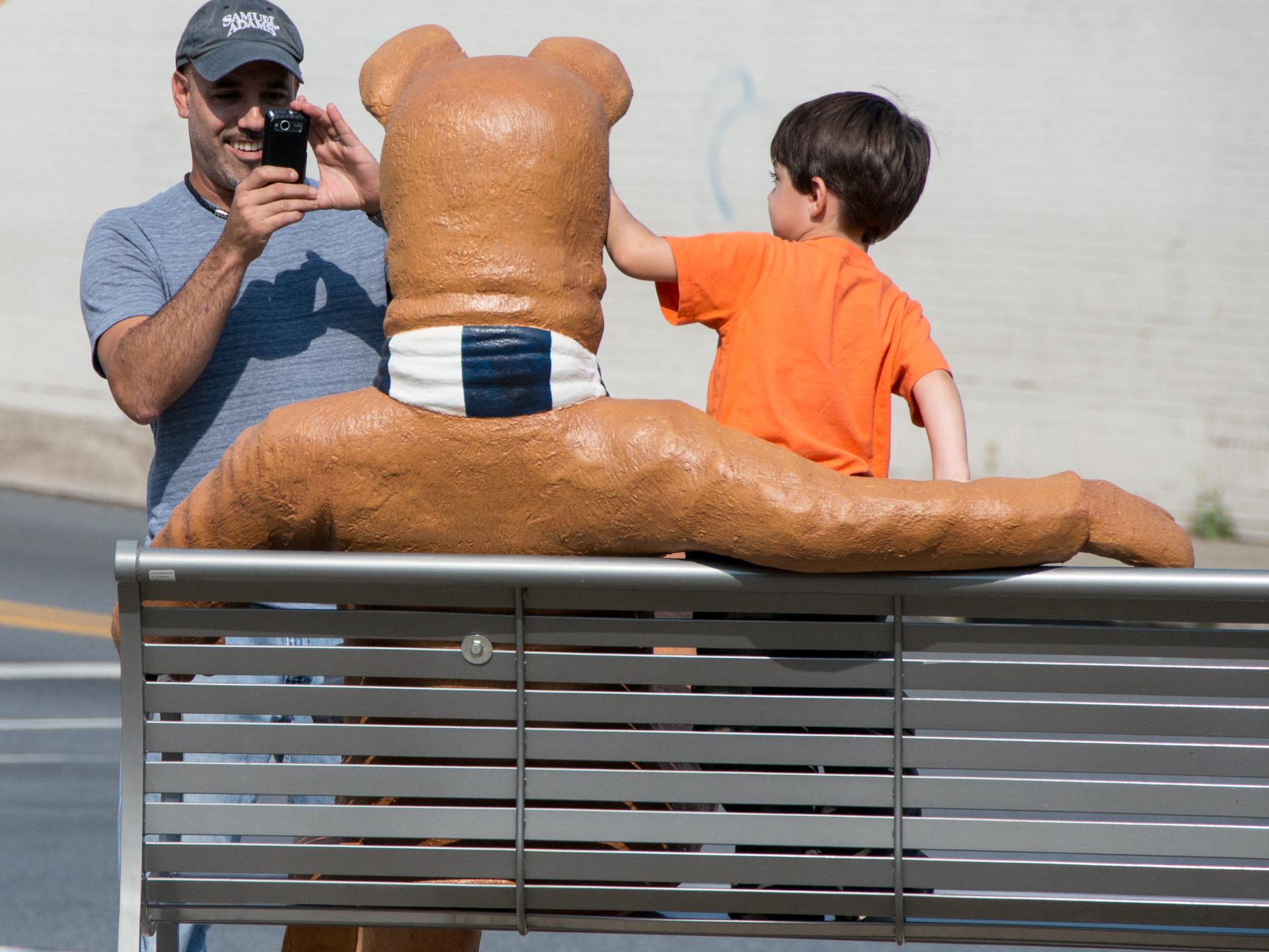 A father takes his son's picture with the Nittany Lion bench.