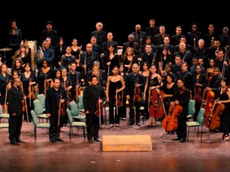 Musicians stand and hold their instruments while they look out from a stage.