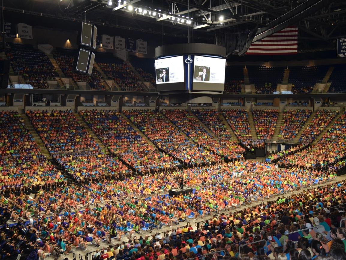 Thousands of students wearing brightly colored teeshirts sit in the BJC 