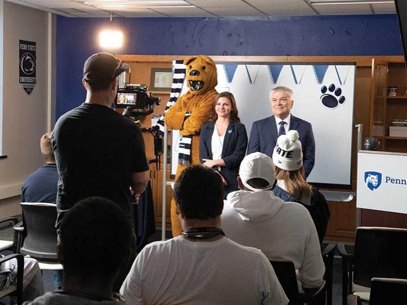 The Nittany Lion poses for a video camera with a female student and President Eric Barron.