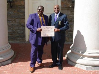 two men standing in front of Old Main holding a certificate