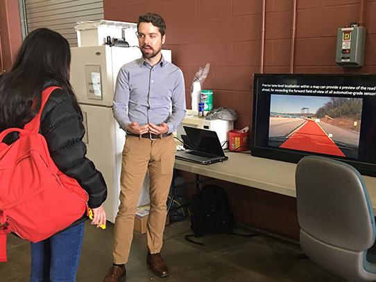 Man speaking with a woman in front of a TV screen.