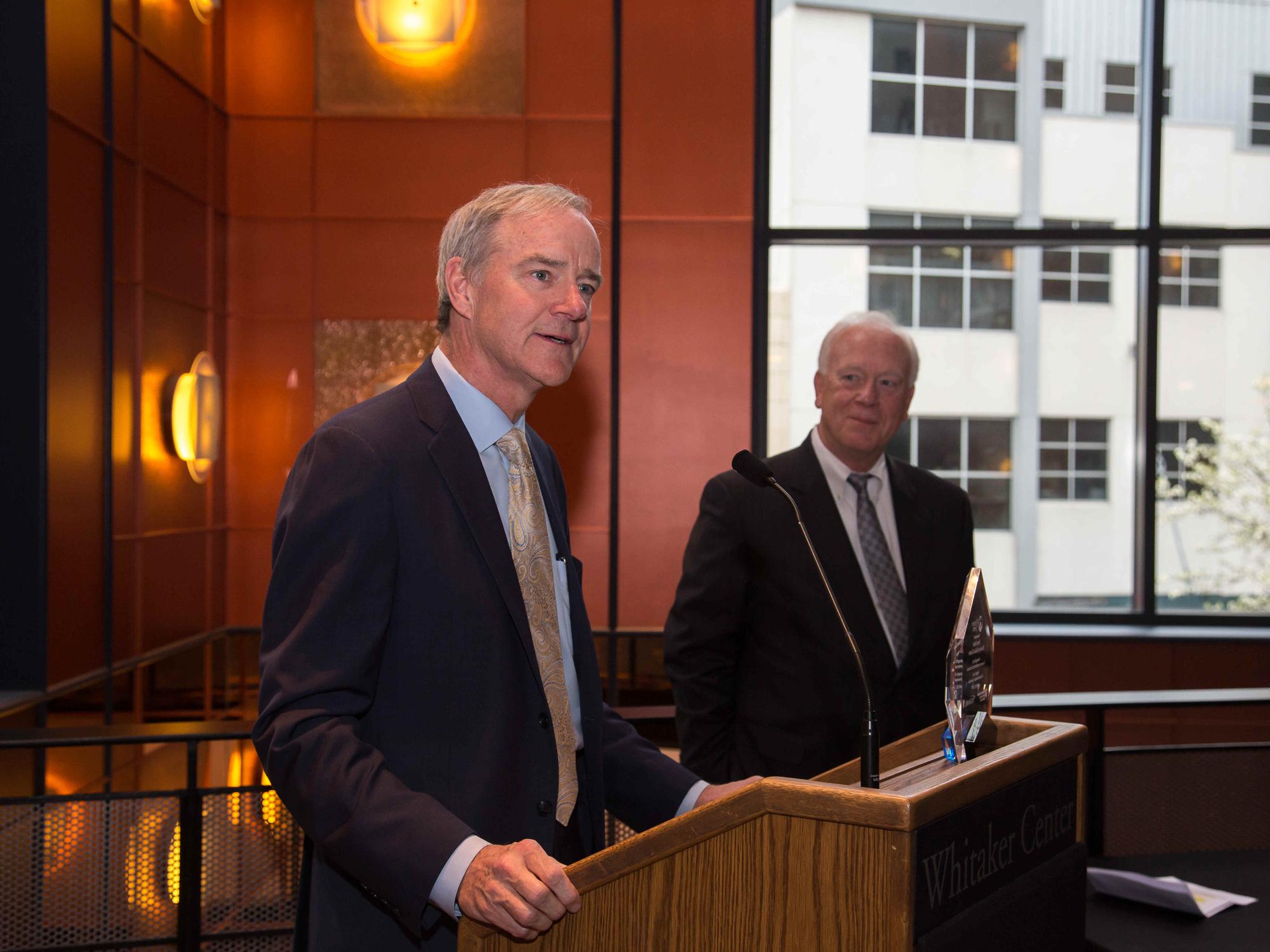 Dr. Peter Dillon accepts an award on behalf of Hershey Medical Center at Surgery Live’s 10th anniversary celebration in 2018. Dillon is wearing a suit and tie and stands behind a podium.