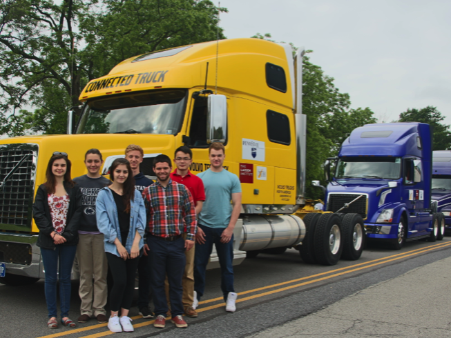 Students from the intelligent systems vehicle group stand in front of a truck platoon.