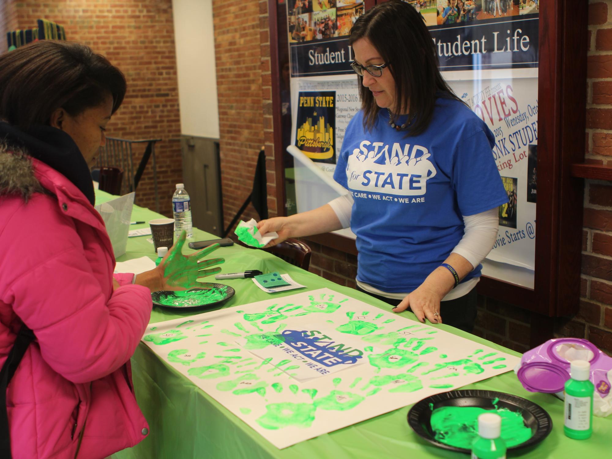 A student prepares to leave a green handprint on a poster
