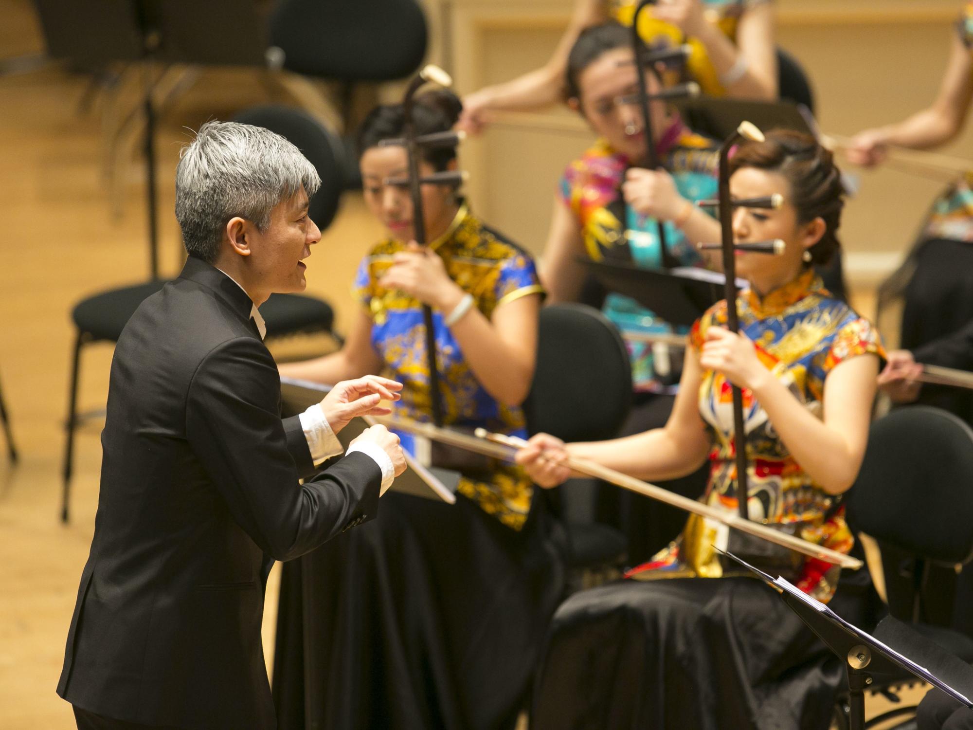 A conductor leads musicians who are playing traditional Chinese instruments.