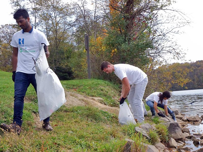 Members of Penn State Positive Energy and Range Resources employees pick up trash along the water at Cross Creek County Park.