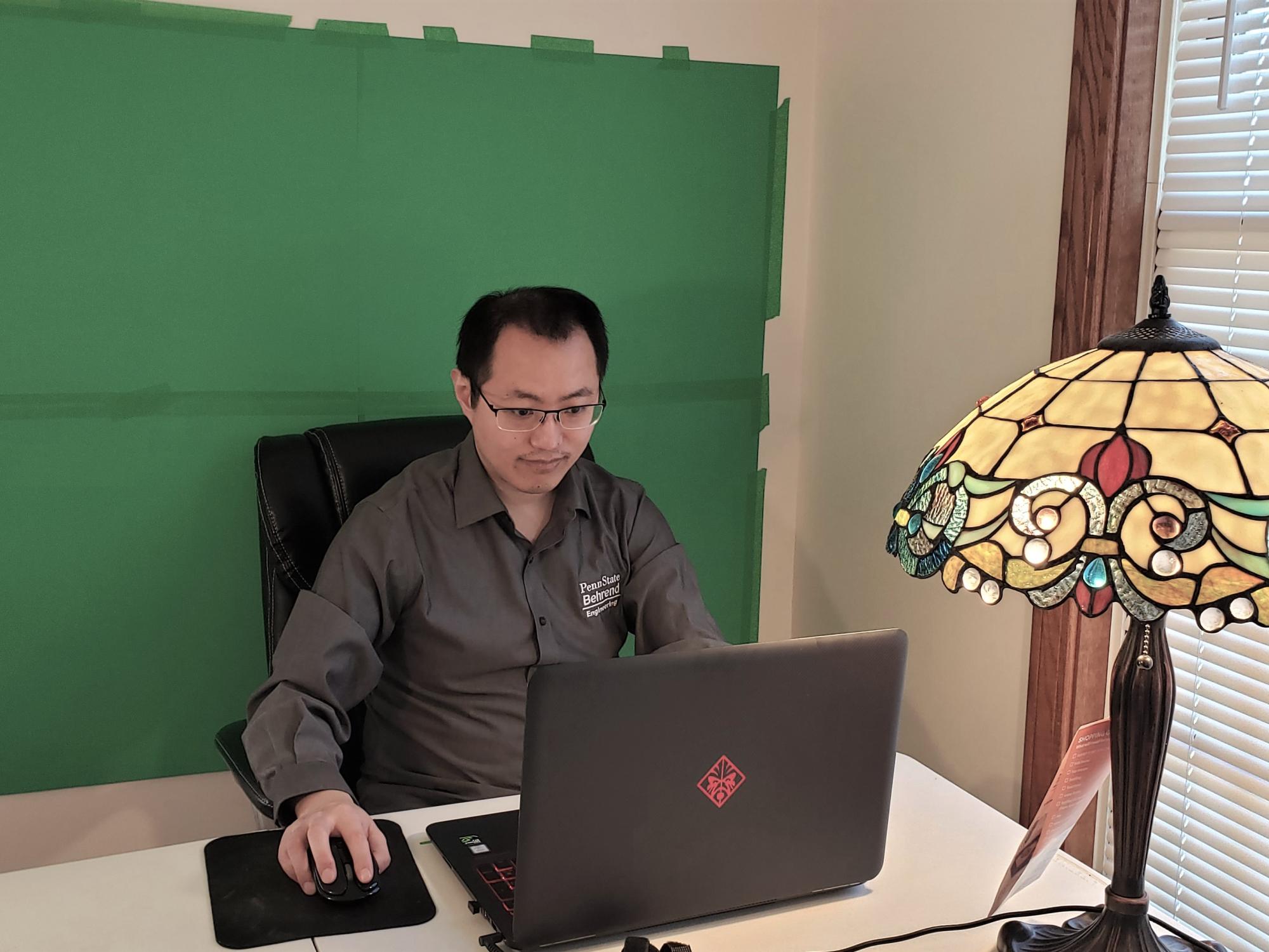 Penn State Behrend professor Richard Zhao works in front of a green screen computer backdrop.