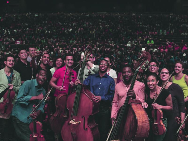Musicians of Sphinx Virtuosi pose with their backs to the audience while an off-frame photographer takes a group photo.