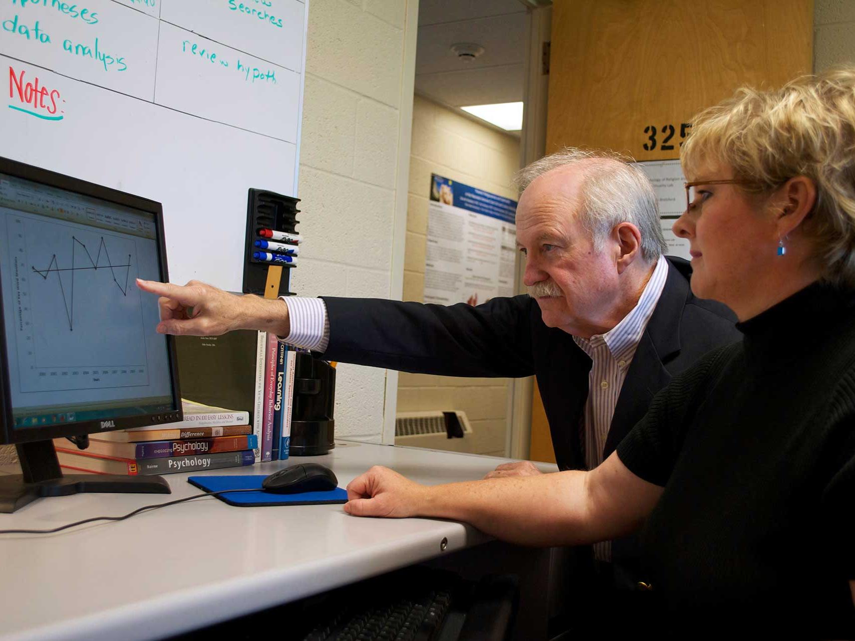 male pointing at graph on screen, woman looking on