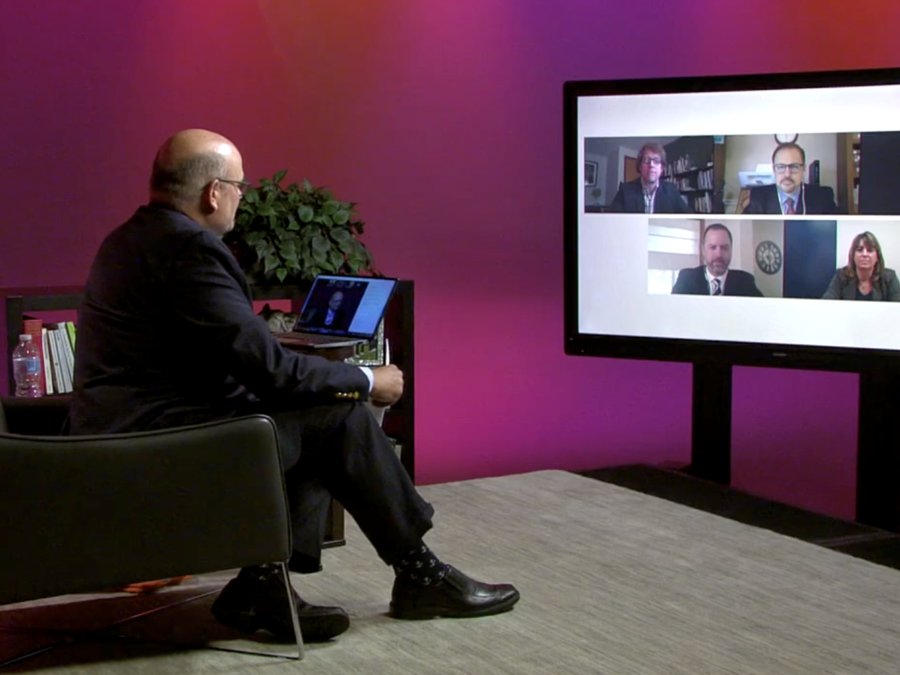 Kevin Snider sits and looks at virtual panelists on television screen