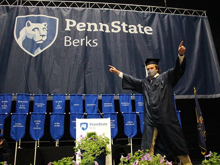 A student crosses the stage, pointing out at the crowd 