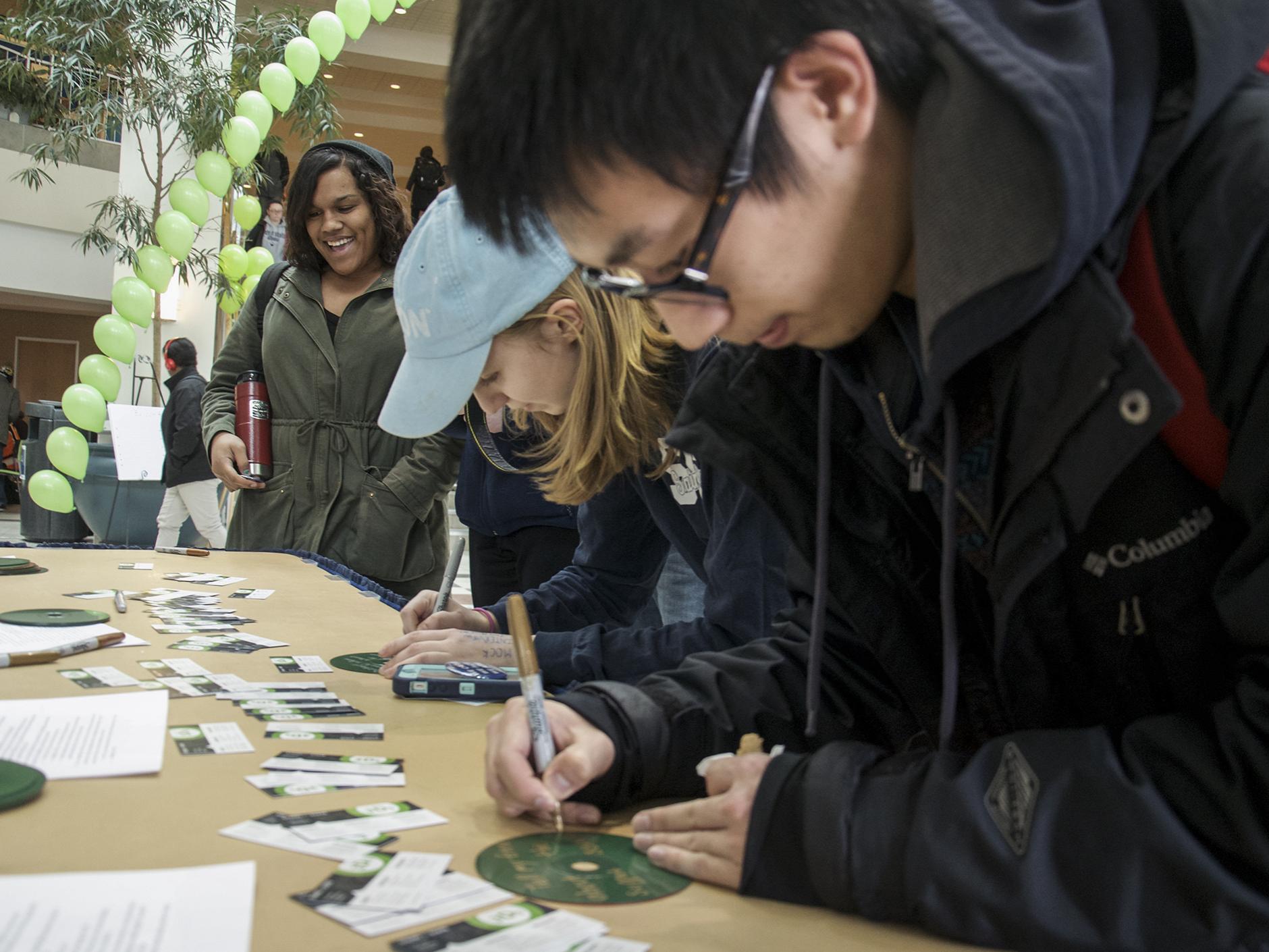 Students writing down messages on green CDs