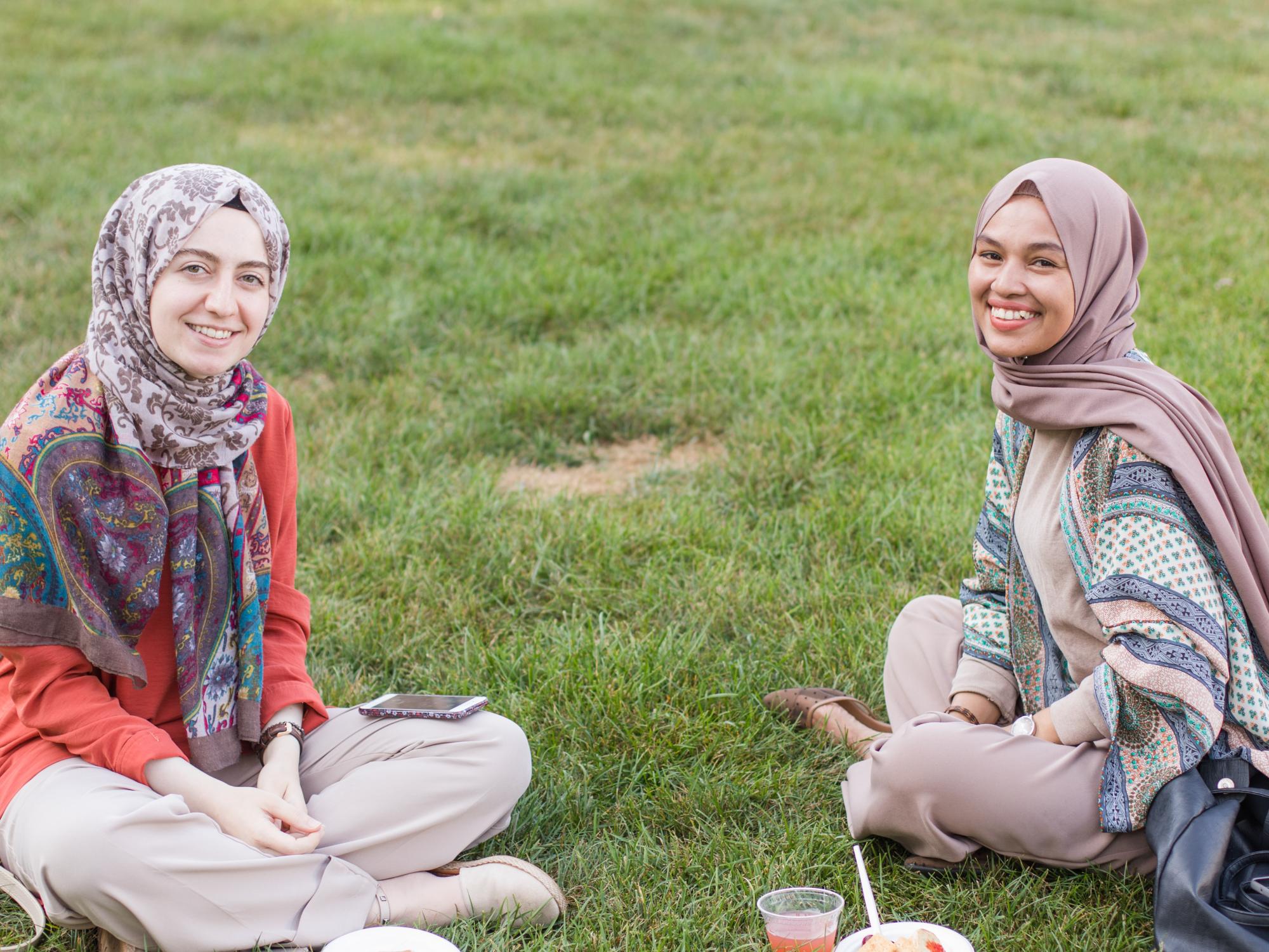 Two international students converse while sitting on Old Main Lawn