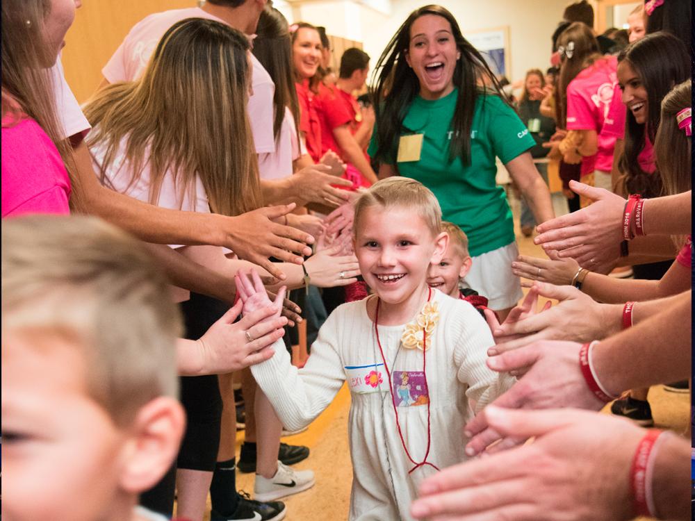 A young child is seen walking through a group of older kids, smiling and giving high-fives.