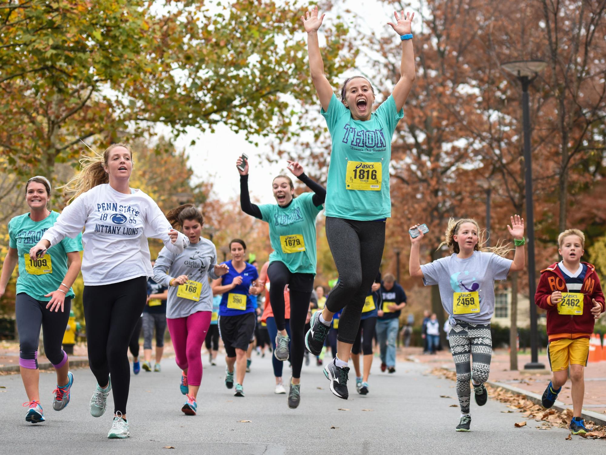 Students run and jump down the street while participating in the THON 5 K