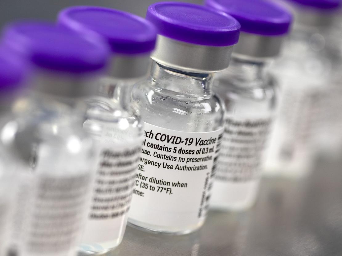 A row of vials displays labels indicating they are COVID-19 vaccine.