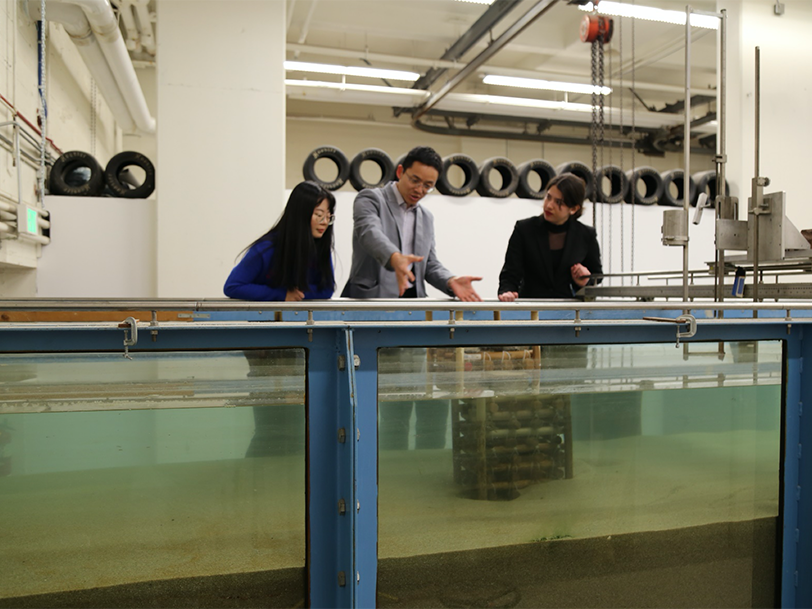 three people stand in front of large tank of water placed in a lab