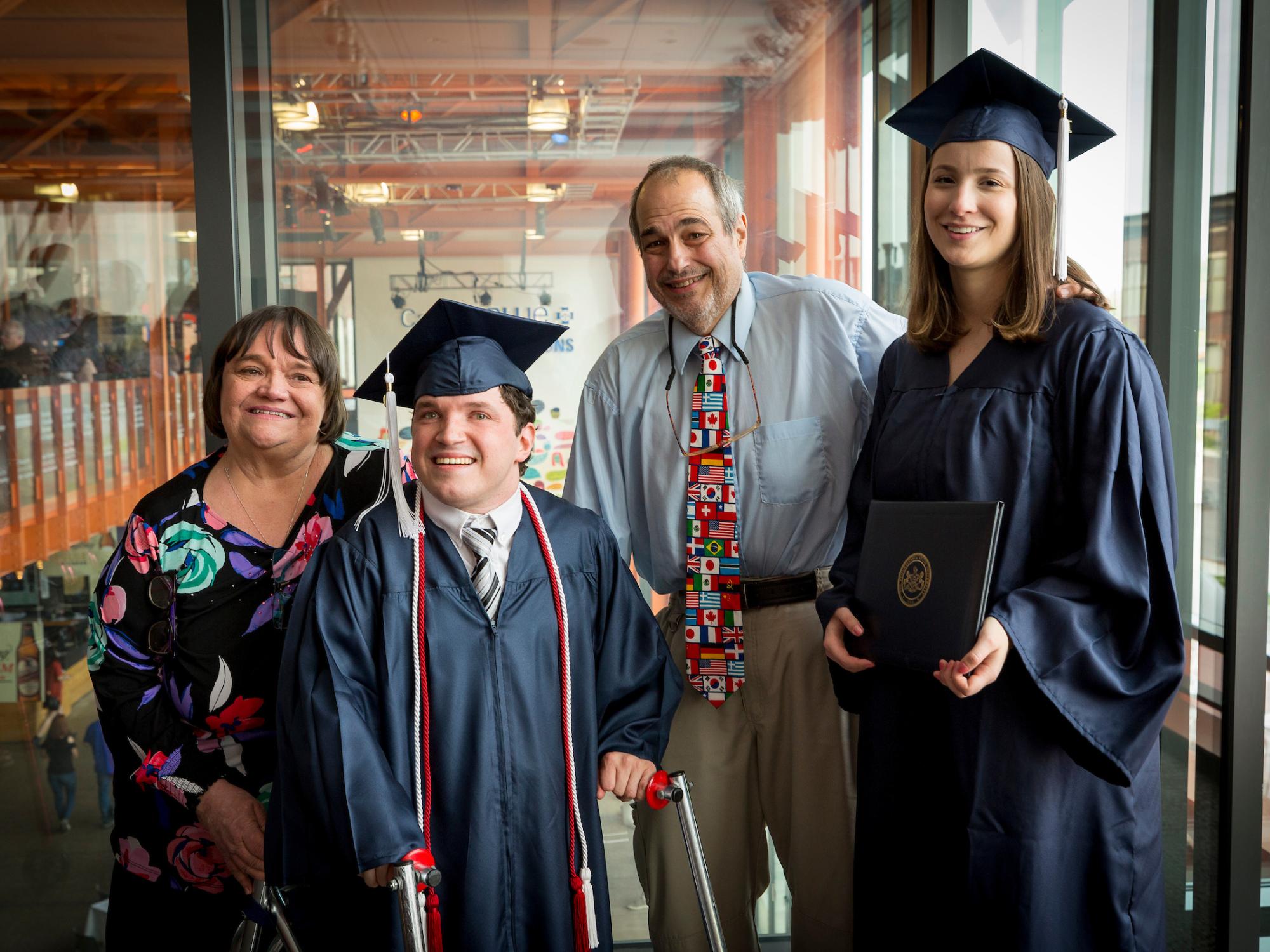 four people standing and smiling, two in caps and gowns